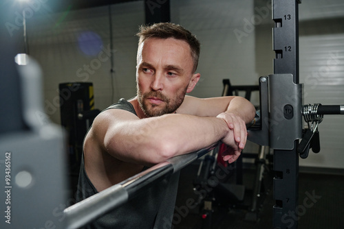 Caucasian brutal man leaning on metal barbell while resting between sets