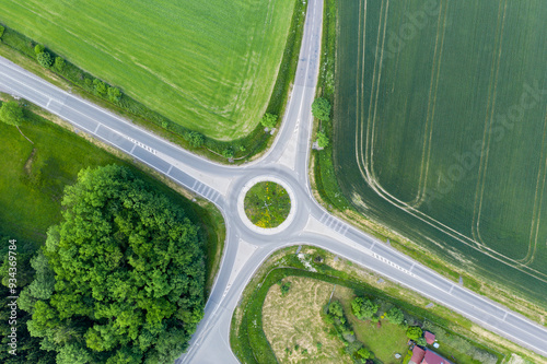 Fototapeta Naklejka Na Ścianę i Meble -  The roundabout road aerial view that newly developed. Summer sunny day. Roundabout on suburban road. Universal road photo. Road in agricultural fields landscape adn small town.