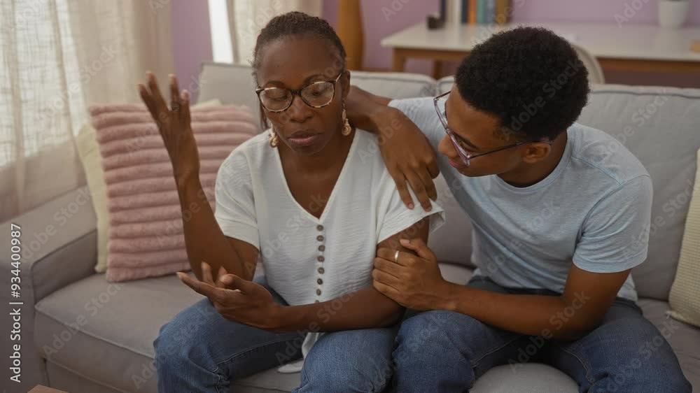 Mother and son sitting together in a living room, with the son consoling the distressed mother, showcasing love and family bonding in their home environment. Mother and son sitting together in a living room, with the son consoling the distressed mother, showcasing love and family bonding in their home environment.