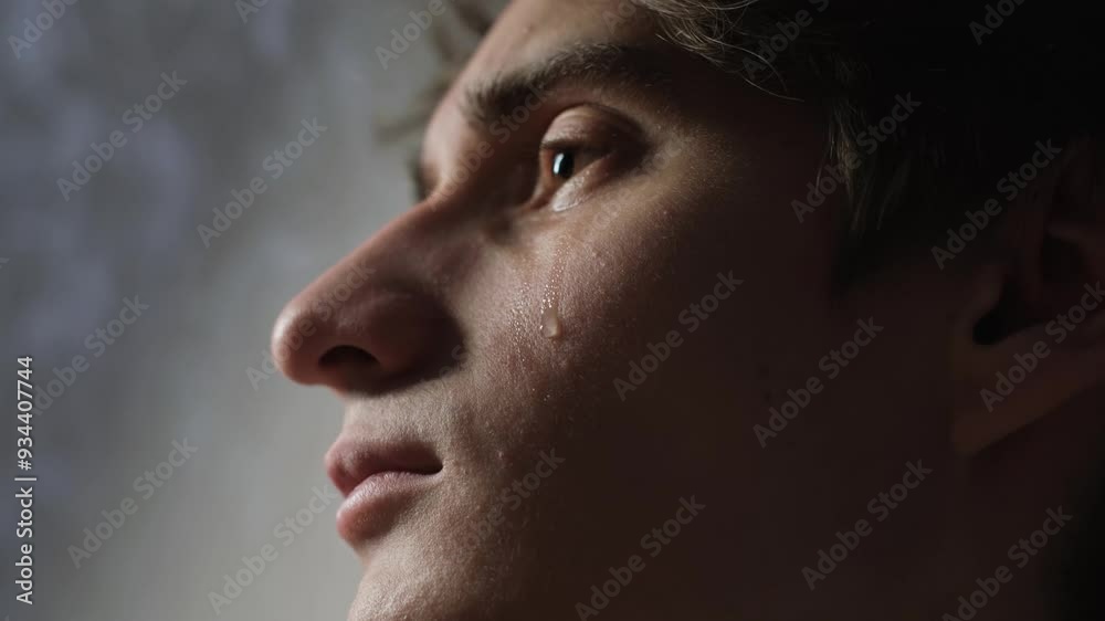 A tear rolls down the cheek of a young man, close-up