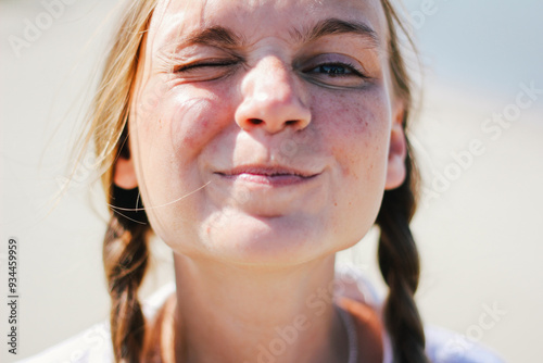 Obraz na płótnie Playful close-up of a young woman with braids, making a funny face while squinting under the bright sun. w salonie