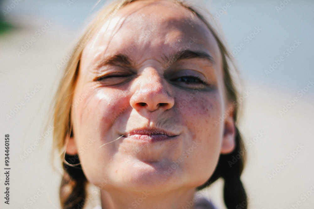 Playful close-up of a young woman with braids, making a funny face while squinting under the bright sun.