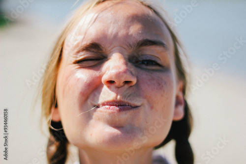 Obraz na płótnie Playful close-up of a young woman with braids, making a funny face while squinting under the bright sun. w salonie
