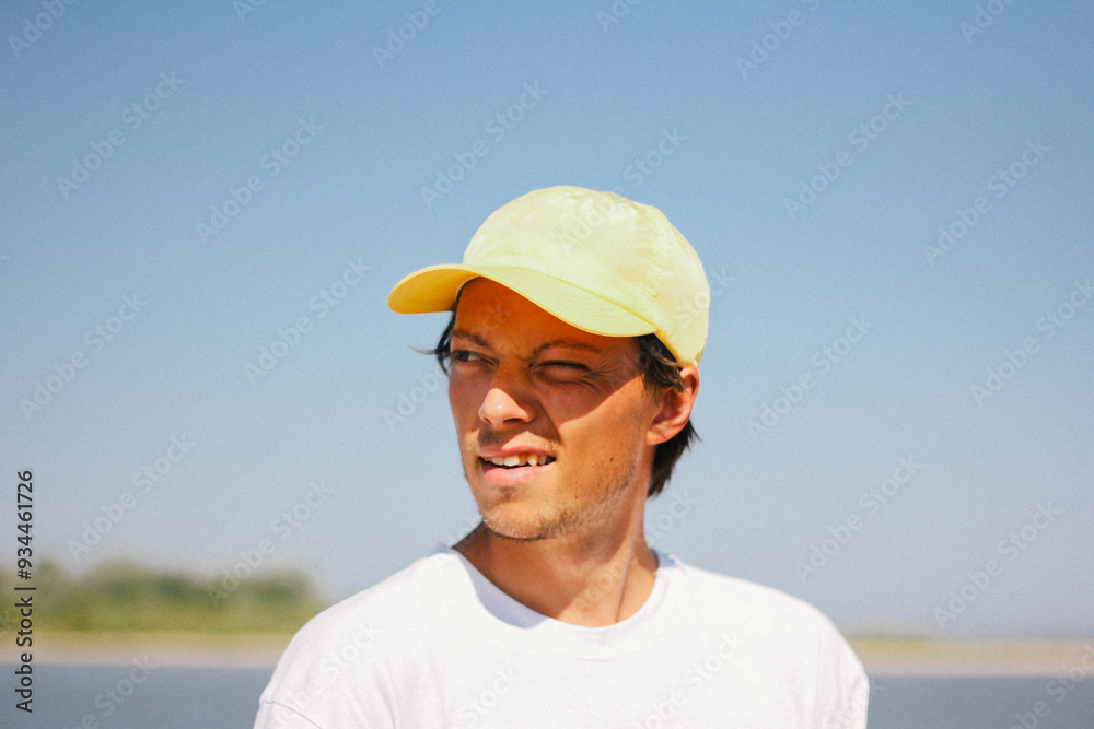 Portrait of a man in a yellow cap enjoying a sunny day outdoors, captured with a squint and a slight smile.