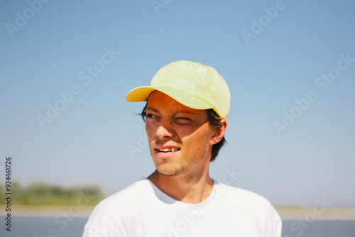 Obraz na płótnie Portrait of a man in a yellow cap enjoying a sunny day outdoors, captured with a squint and a slight smile. w salonie