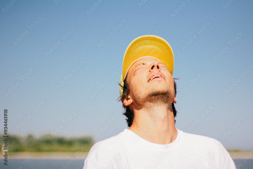 Portrait of a man in a yellow cap enjoying a sunny day outdoors, captured with a squint and a slight smile.