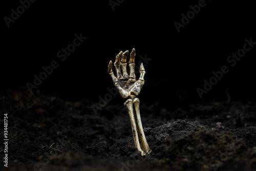 A skeleton hand emerges from dirt and soil as if from underground - reaching up towards the sky, isolated on black background photo