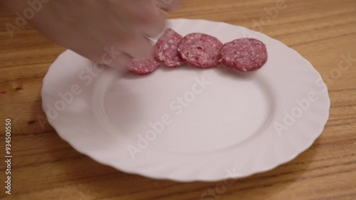 Preparing an antipasti dish. Closeup view of a man hands laying salami, gruyere cheese and german leberwurst in a white dish