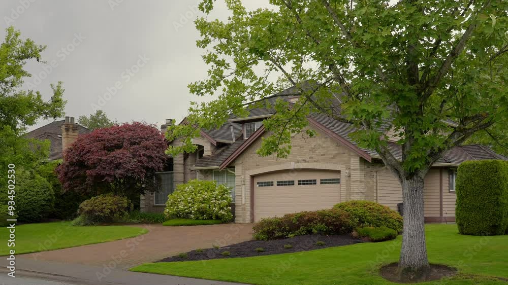 Establishing shot of two story stucco luxury house with big tree and nice landscape at spring rainfall in Vancouver, Canada, North America. Day time on June 2024. ProRes 422 HQ.