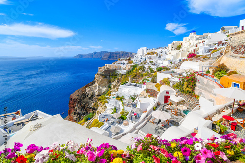 The blue dome church, whitewashed village and blue Aegean Sea are visible from a terrace with flowers in the town of Oia on the island of Santorini Greece.