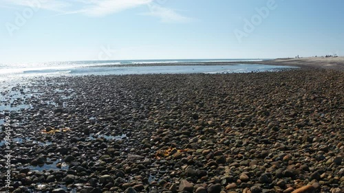 Flying low above the rocky shoreline into the reflecting sun at Trestles beach