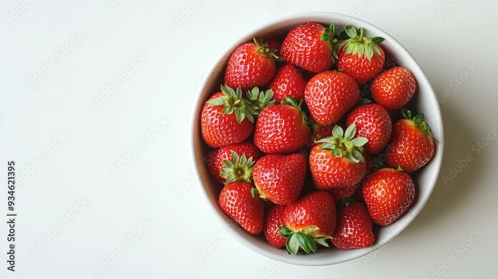 A white bowl filled with red ripe strawberries on a light white background. The minimalistic setting makes the vibrant color of the berries pop. A white bowl filled with red ripe strawberries on a light white background. The minimalistic setting makes the vibrant color of the berries pop.