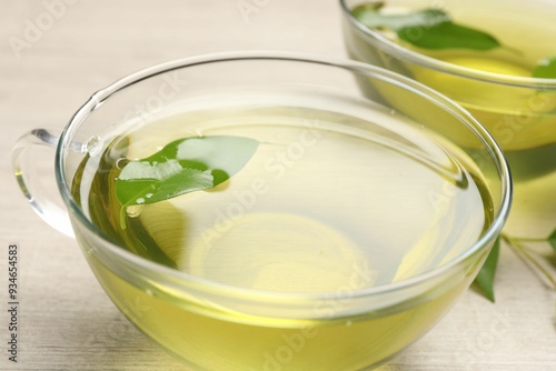 Refreshing green tea in cups and leaves on wooden table, closeup