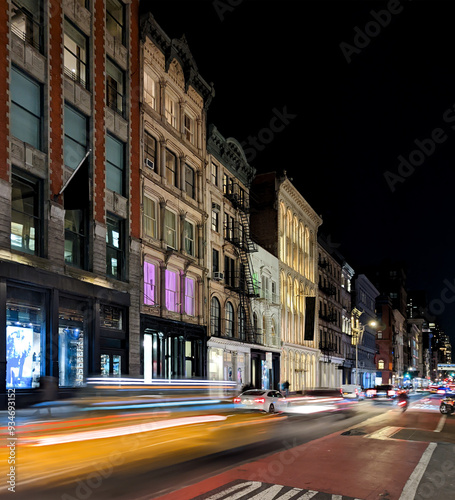Yellow taxi with motion blur effect driving past the historic buildings on Broadway in the SoHo neighborhood of New York City at night