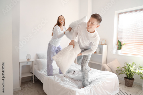 Young woman with her husband fighting pillows in bedroom