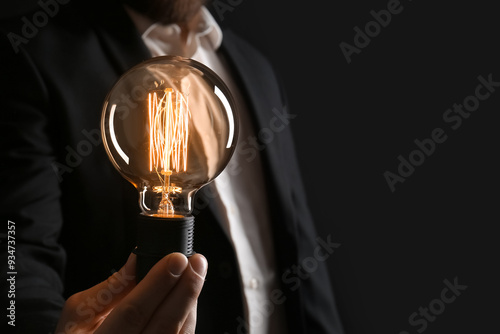 Businessman holding glowing light bulb on black background, closeup