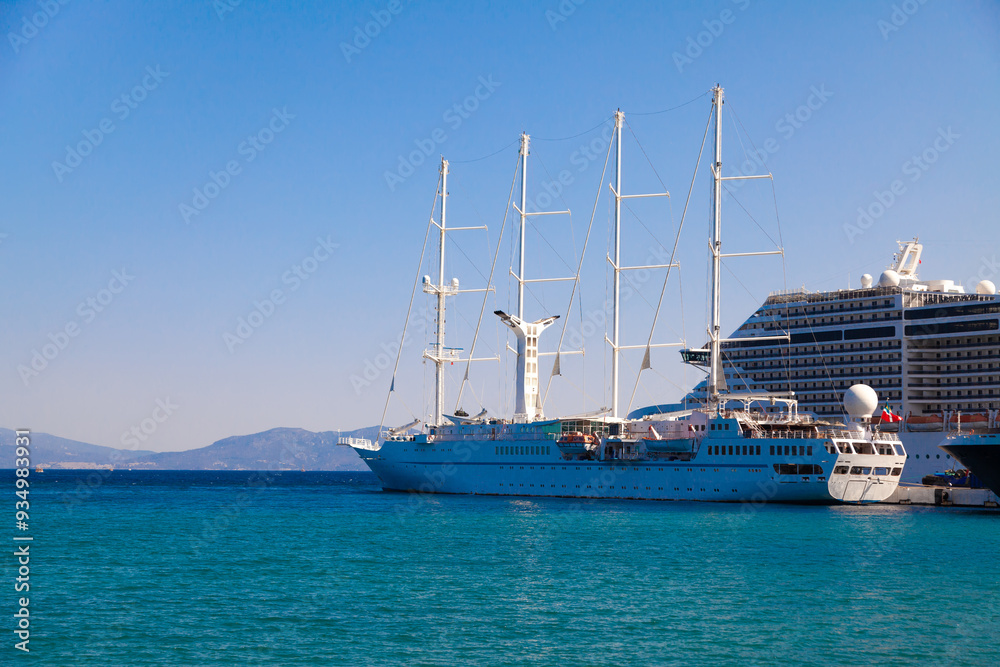Large cruise ships and a sailboat are docked at the pier against the blue sea on a clear summer day. Ideal for content about maritime tourism and sailing. Large cruise ships and a sailboat are docked at the pier against the blue sea on a clear summer day. Ideal for content about maritime tourism and sailing.