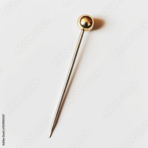 A single, shiny, gold-headed pin lies on a white background.