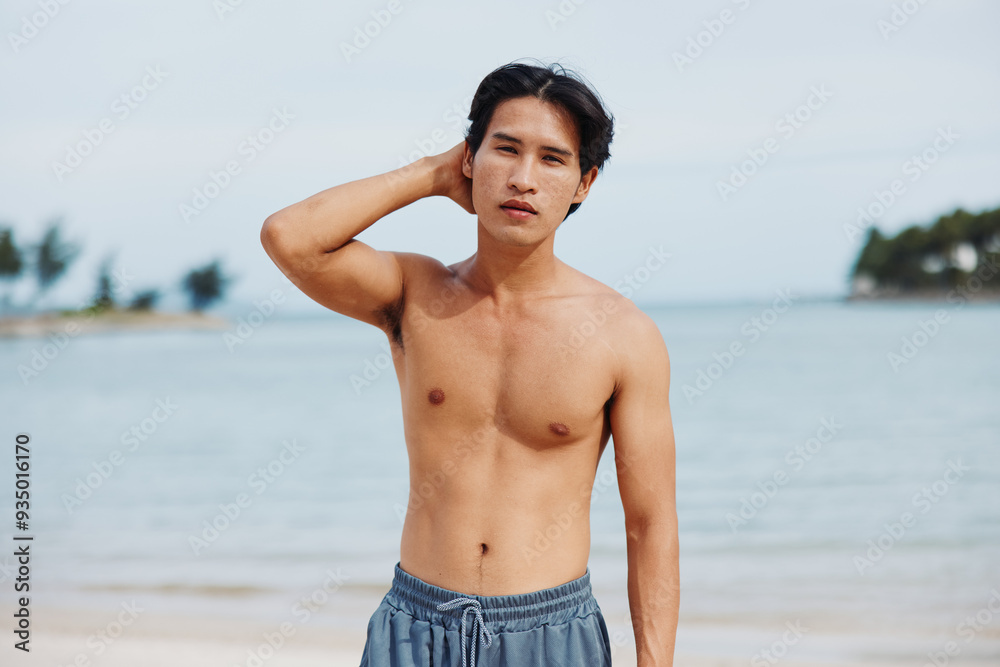Smiling Asian Man Enjoying Tropical Beach Vacation: Muscular Torso on the Sand and Palm Trees in Background Smiling Asian Man Enjoying Tropical Beach Vacation: Muscular Torso on the Sand and Palm Trees in Background