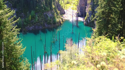 Sunken forest of Lake Kaindy in Kazakhstan. Beautiful mountain natural landscape. A blue lake with tree trunks sticking out of it. Panoramic view of the reserve.