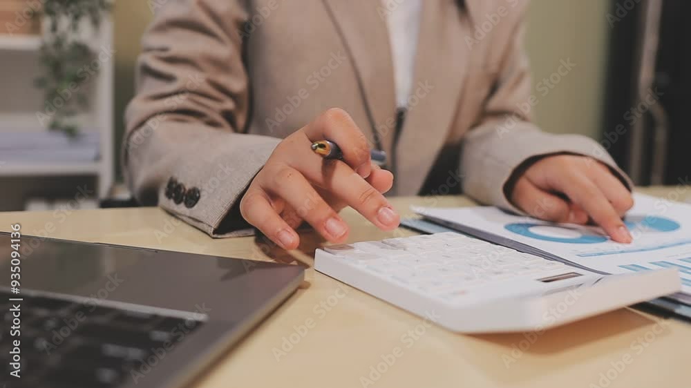 A woman is using a calculator and pen on a desk. She is focused on her work and she is in a serious mood A woman is using a calculator and pen on a desk. She is focused on her work and she is in a serious mood