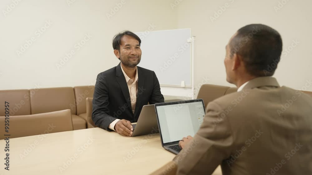 Description: Two businessmen sitting across from each other in an office, engaged in a friendly conversation. Both have laptops in front of them, suggesting a collaborative work environment.
Description: Two businessmen sitting across from each other in an office, engaged in a friendly conversation. Both have laptops in front of them, suggesting a collaborative work environment.