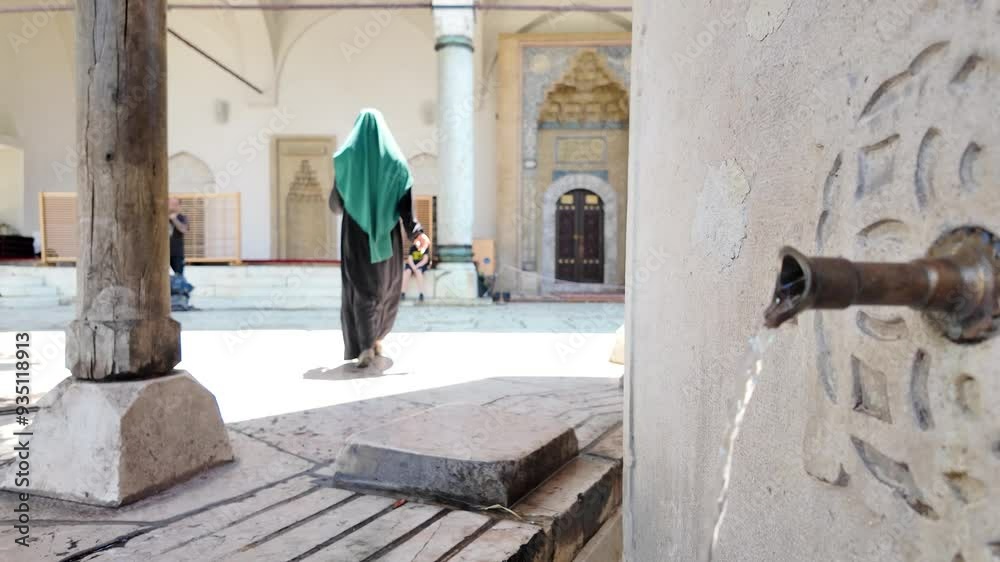 Woman with hijab walking in the courtyard of the Gazi Husrev Bey's Madrasa in Sarajevo, Bosnia Herzegovina. Slow motion. Water flows from the fountain. Woman with hijab walking in the courtyard of the Gazi Husrev Bey's Madrasa in Sarajevo, Bosnia Herzegovina. Slow motion. Water flows from the fountain.