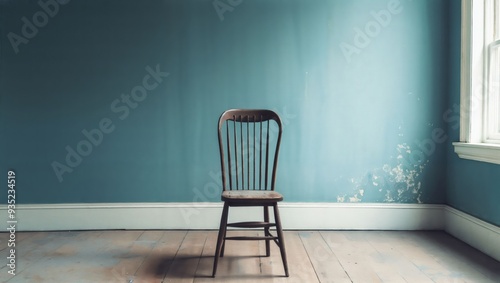 A solitary wooden chair stands against a calming blue wall, evoking feelings of solitude and contemplation, illuminated by soft natural light streaming through a window. photo