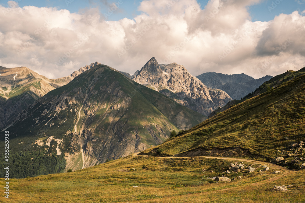Majestic mountains rise in the background, surrounded by lush green hills and billowing clouds under a bright sky. Majestic mountains rise in the background, surrounded by lush green hills and billowing clouds under a bright sky.