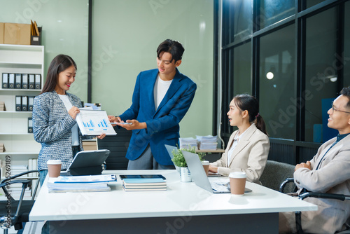 In a boardroom, an Asian team meets at a desk, presenting financial terms and strategies. Executives and employees collaborate, sharing ideas and work guidelines for success during an annual meeting.