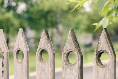 A fragment of a wooden decorative peaked old fence, summer country side green background, selective focus.