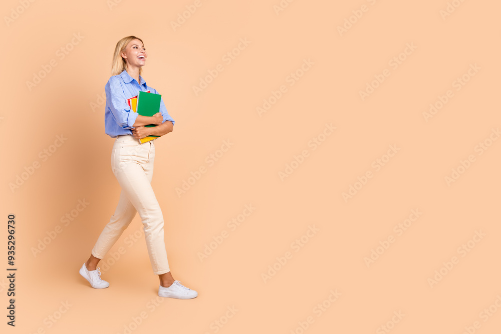 Full length photo of adorable lovely girl wear blue shirt holding copybooks walking looking empty space isolated beige color background Full length photo of adorable lovely girl wear blue shirt holding copybooks walking looking empty space isolated beige color background