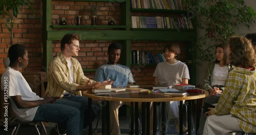 A man is talking to his friends while sitting at a table indoors. He opens the Bible. Bible Study Club