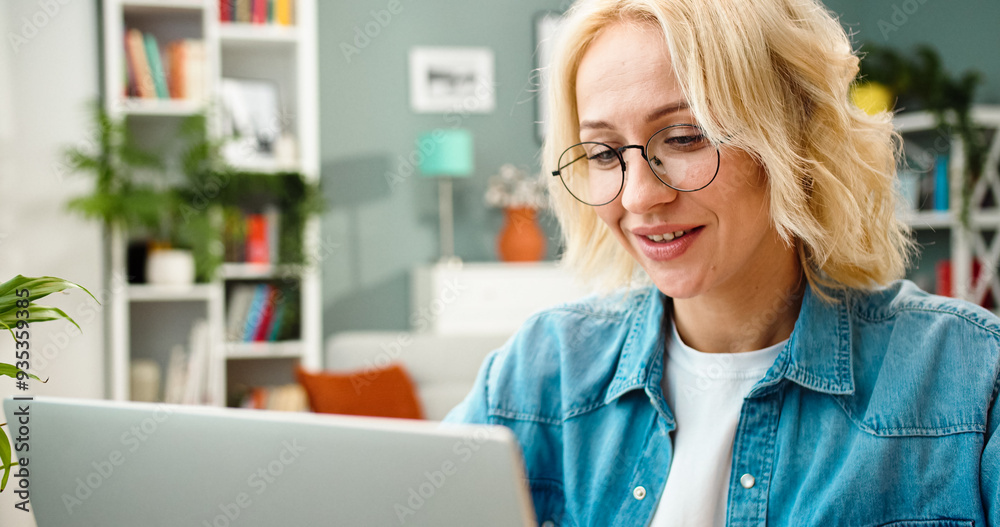 Close up portrait of beautiful young Caucasian female wearing glasses sits in front of laptop screen. Satisfied woman surfs internet at home. Close up portrait of beautiful young Caucasian female wearing glasses sits in front of laptop screen. Satisfied woman surfs internet at home.