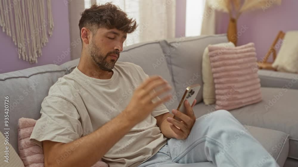 Young man sitting in a living room holding his phone while suffering from neck pain on a comfortable couch in a cozy and modern home interior Young man sitting in a living room holding his phone while suffering from neck pain on a comfortable couch in a cozy and modern home interior