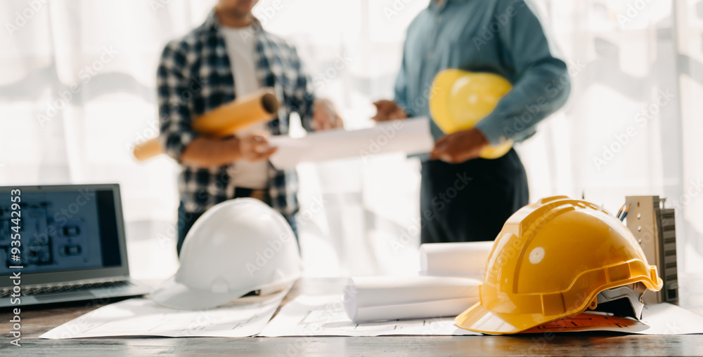 Engineer desk with object paper and tablet with blurry engineer teamwork hardworking to consults about their building project.. Engineer desk with object paper and tablet with blurry engineer teamwork hardworking to consults about their building project..