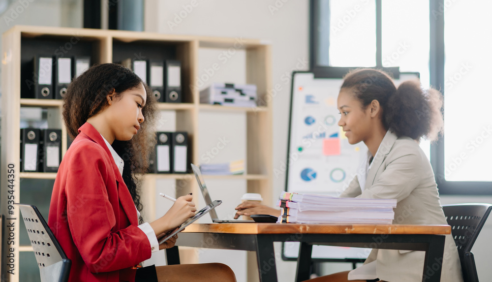 Business African women work and discuss their business plans. A Human employee explains and shows her colleague the results paper in office.. Business African women work and discuss their business plans. A Human employee explains and shows her colleague the results paper in office..