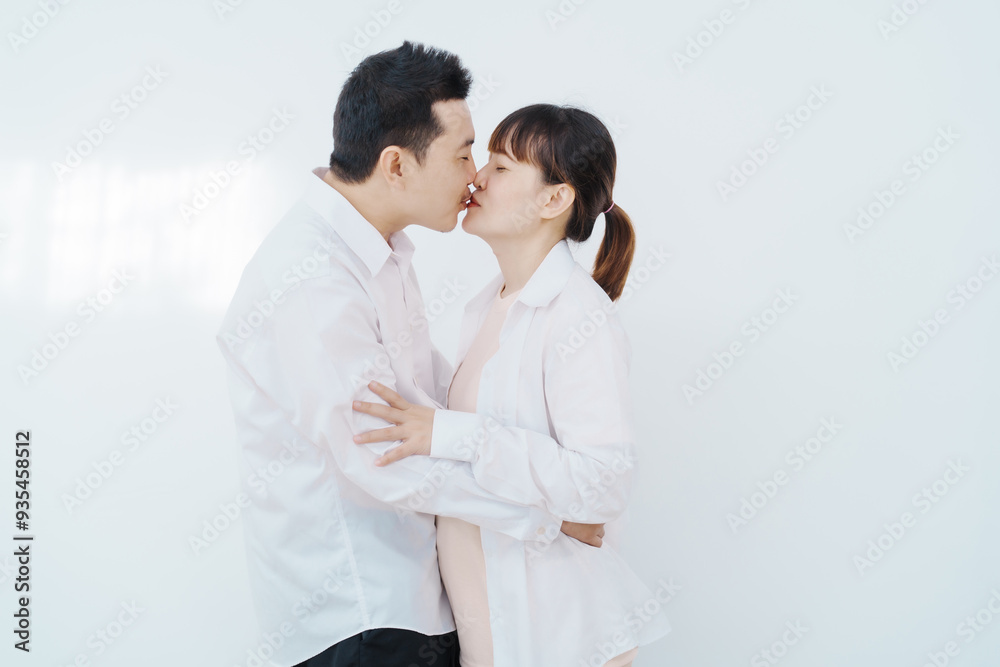 A happy Asian couple, expecting a baby, embraces in a cozy living room. The pregnant woman smiles warmly, while the man lovingly supports her, capturing a moment of joyful anticipation. A happy Asian couple, expecting a baby, embraces in a cozy living room. The pregnant woman smiles warmly, while the man lovingly supports her, capturing a moment of joyful anticipation.