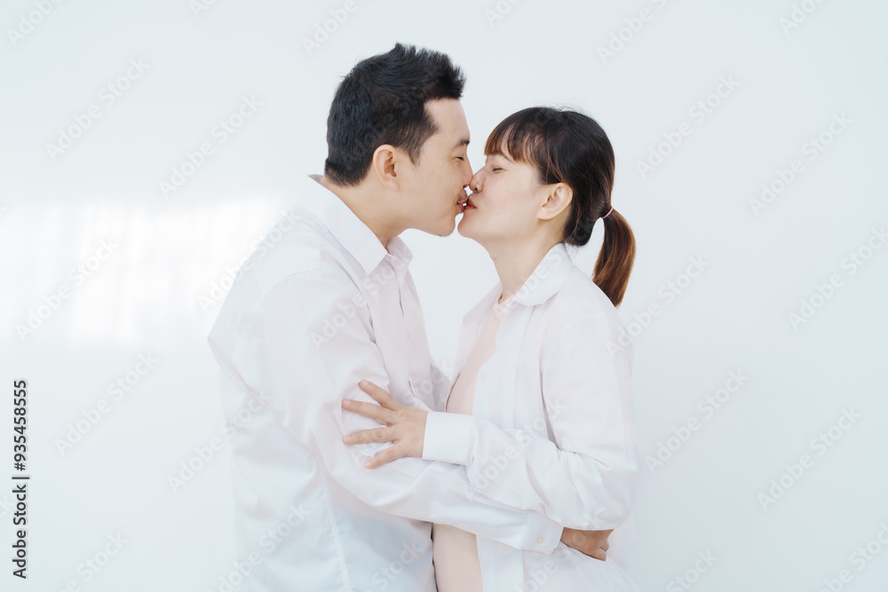 A happy Asian couple, expecting a baby, embraces in a cozy living room. The pregnant woman smiles warmly, while the man lovingly supports her, capturing a moment of joyful anticipation. A happy Asian couple, expecting a baby, embraces in a cozy living room. The pregnant woman smiles warmly, while the man lovingly supports her, capturing a moment of joyful anticipation.