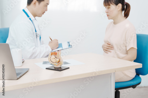 Asian female doctor listens to belly of pregnant mother during a prenatal exam in clinic. doctor provides caring advice, ensuring the health and happiness of the expecting mother and baby.