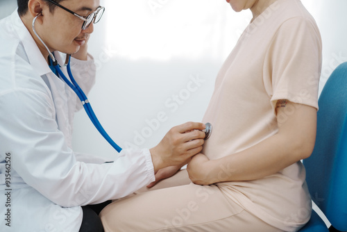 Asian female doctor listens to belly of pregnant mother during a prenatal exam in clinic. doctor provides caring advice, ensuring the health and happiness of the expecting mother and baby.