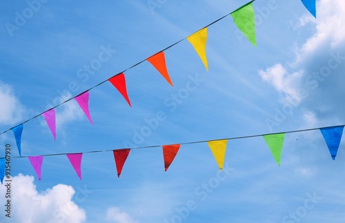 Colorful triangular pennant flags or bunting flags strung across a blue sky with clouds 