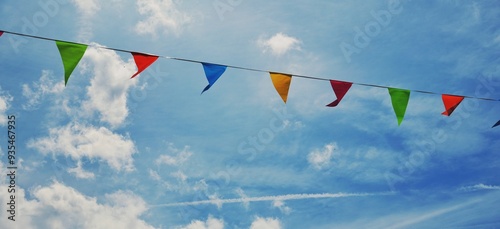 Colorful triangular pennant flags or bunting flags strung across a blue sky with clouds 