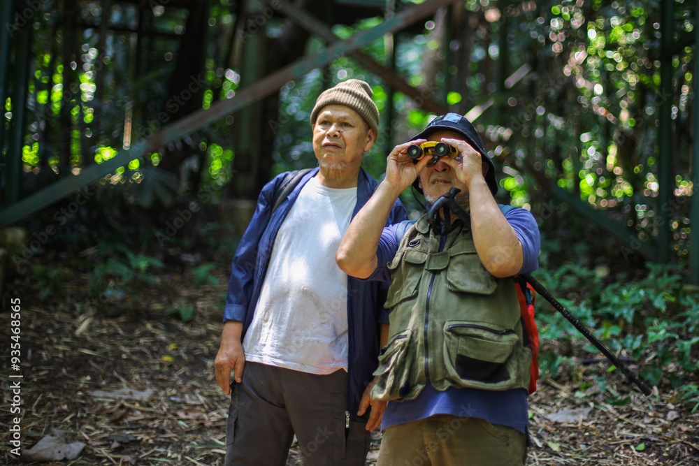 Fototapeta premium Two Asian Senior Man Looking At The View Using Binoculars While Hiking And Trekking