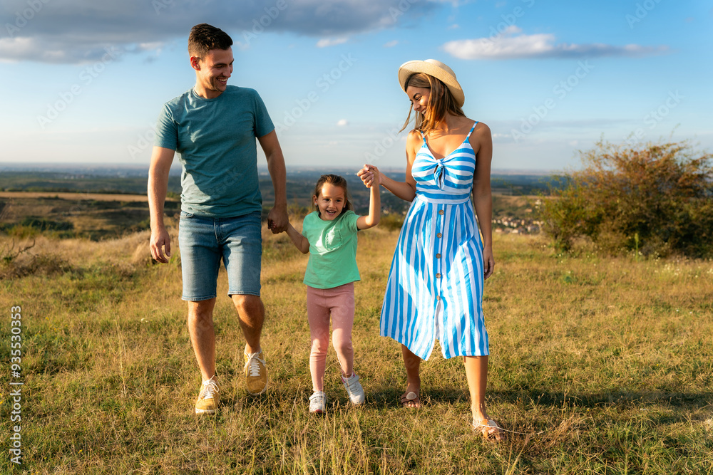 Mother and father are holding their daughter's hands as they walk through the field, having fun and laughing Mother and father are holding their daughter's hands as they walk through the field, having fun and laughing