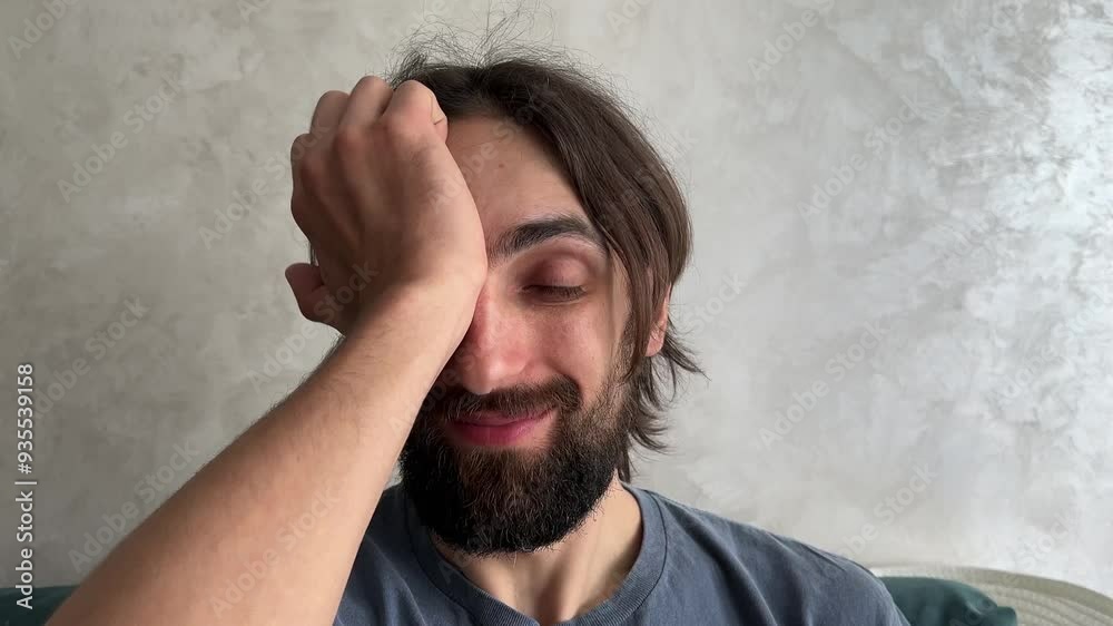 Bearded man covers and uncovers his eyes with his hand, expressing various emotions and gestures in a contemplative manner Bearded man covers and uncovers his eyes with his hand, expressing various emotions and gestures in a contemplative manner