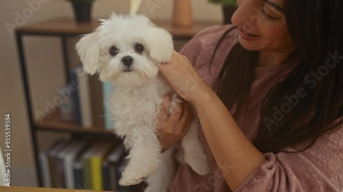 A young woman lovingly holds a small fluffy white bichon maltese dog at home, depicting companionship. photo