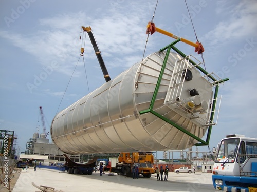 A large tank being lifted by a crane at an industrial site. The image showcases the heavy lifting and precision required in industrial operations.