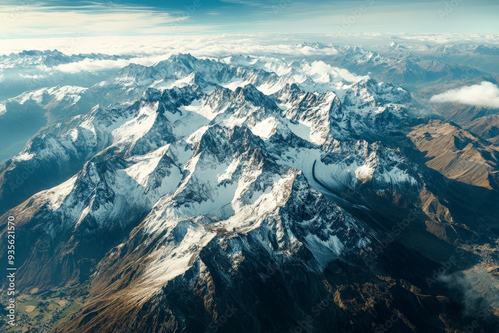 Obraz premium A beautiful aerial landscape of a snow-covered mountain range under a partly cloudy sky, capturing the pristine and rugged beauty of the natural terrain.