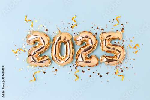 2025 New Year holidays concept. Golden inflatable balloons, ribbons and glittering stars confetti on a blue background.